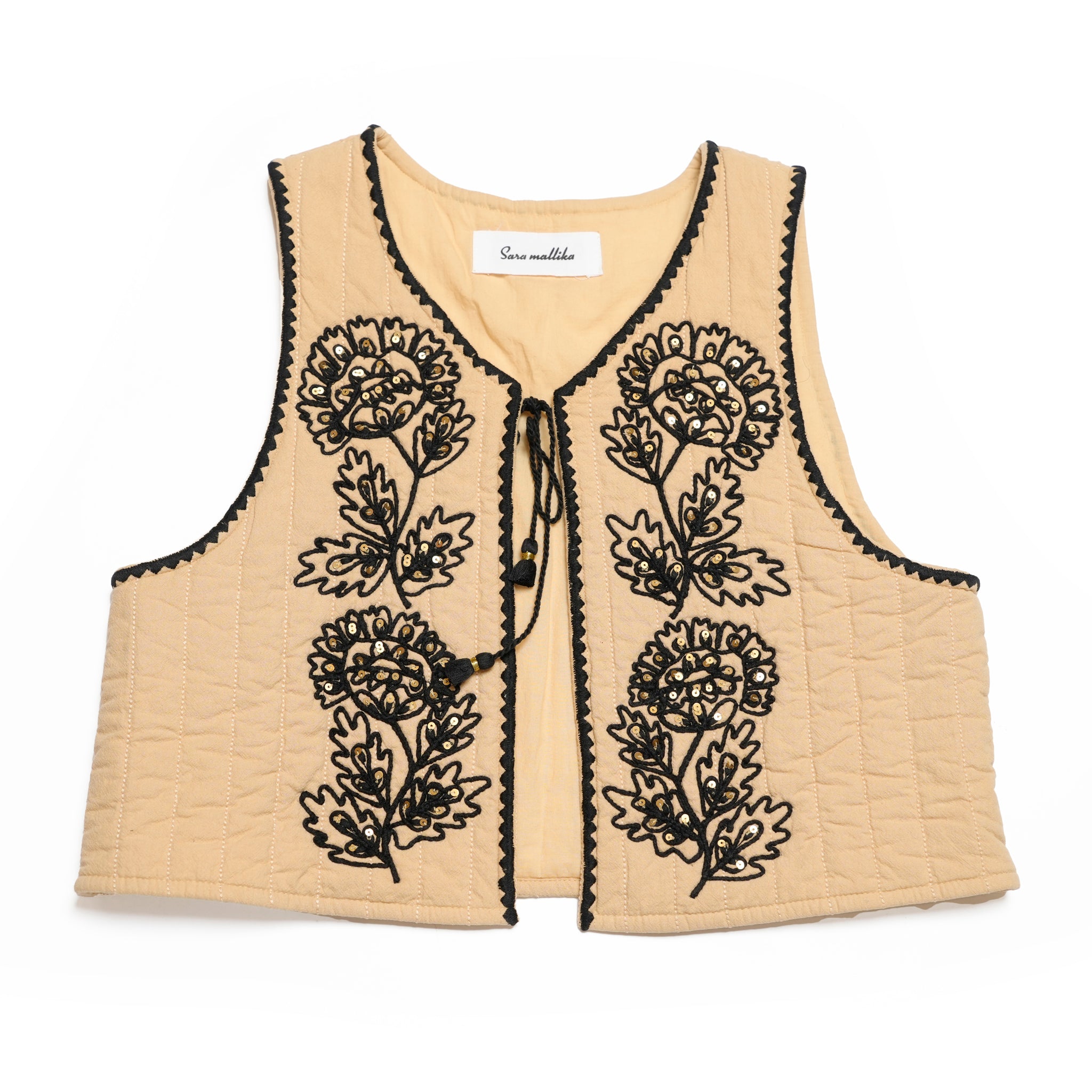 SARA MALLIKAのベージュのコットンドリ刺繍キルティングベスト。大きなタッセルと紐リボンが特徴的な秋にぴったりの軽やかな一枚。
